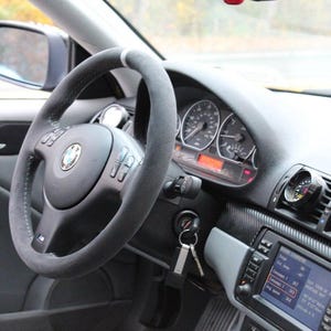 K&ouml;nnte beinhalten: Das Innere eines Autos mit einem schwarzen Lederlenkrad, einem Armaturenbrett aus Kohlefaser und Nachr&uuml;st-Instrumenten. Das Auto hat eine graue Innenausstattung und ein schwarzes Lederlenkrad.