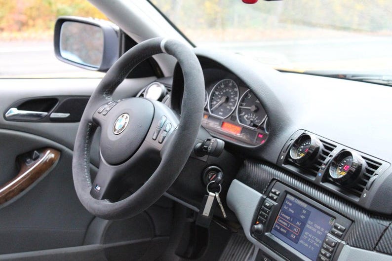 K&ouml;nnte beinhalten: Das Innere eines Autos mit einem schwarzen Lederlenkrad, einem Armaturenbrett aus Kohlefaser und Nachr&uuml;st-Instrumenten. Das Auto hat eine graue Innenausstattung und ein schwarzes Lederlenkrad.
