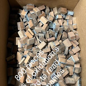 May include: A cardboard box filled with hundreds of small, rectangular wooden blocks. Many blocks have metal plates attached. The text on the side of the box reads: "800 pieces Lots of oxidation's Hard to read companies."
