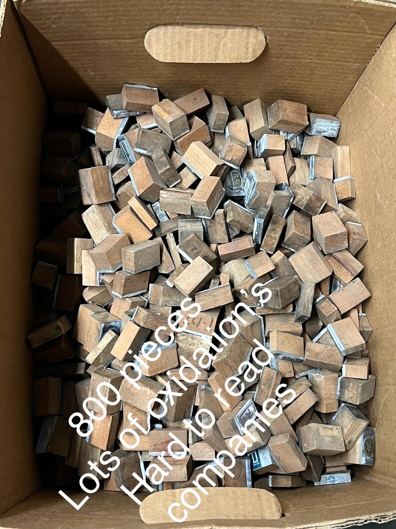 May include: A cardboard box filled with hundreds of small, rectangular wooden blocks. Many blocks have metal plates attached. The text on the side of the box reads: "800 pieces Lots of oxidation's Hard to read companies."