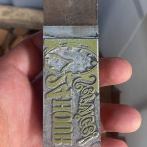 May include: A rectangular metal printing block with the words "4 Hour Service" and "Tennice" in a stylized font. The block has a green and silver design with a clock face.