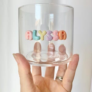 May include: A clear glass cup with the name "ALYSSA" spelled out in colorful, bubble-shaped letters.