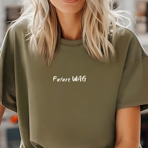 May include: A woman wearing a green oversized t-shirt with the text "Future WAG" printed in white on the front. She is wearing blue jeans with distressed details.