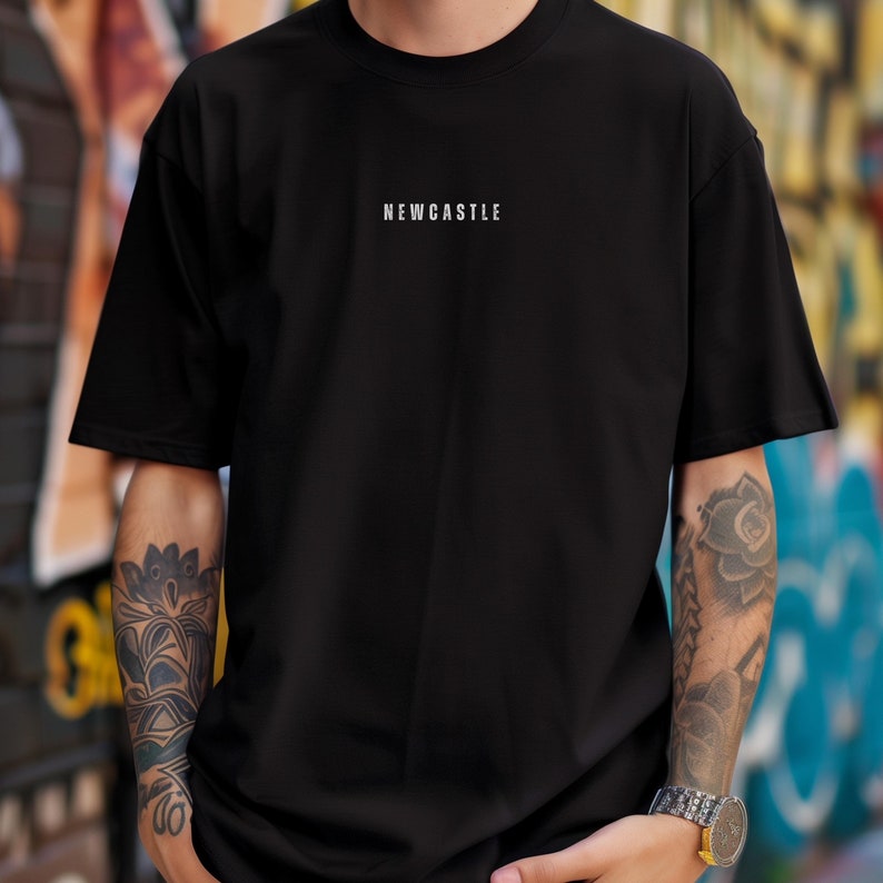 K&ouml;nnte beinhalten: Schwarzes T-Shirt mit dem Wort "NEWCASTLE" in Wei&szlig; auf der Vorderseite.