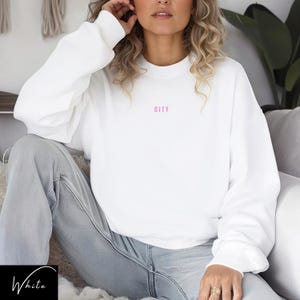 May include: White sweatshirt with long sleeves and a pink "CITY" graphic on the front.