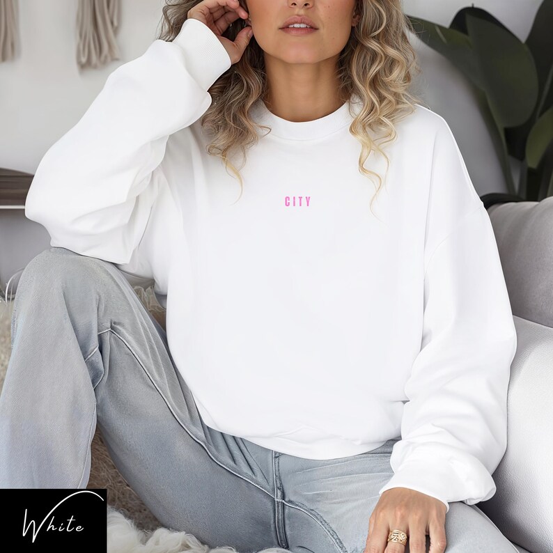 May include: White sweatshirt with long sleeves and a pink "CITY" graphic on the front.