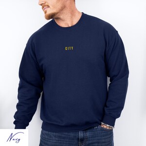 May include: A navy blue sweatshirt with the word "CITY" embroidered in yellow on the chest.