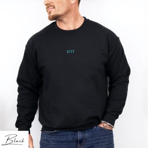 May include: Black long-sleeved sweatshirt with the word "CITY" printed in teal on the front.