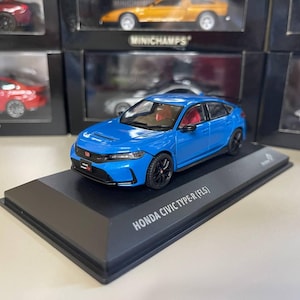 Può includere: Modellino blu di una Honda Civic Type-R (FL5). Il modello è esposto su un supporto nero con il nome dell'auto. L'auto ha ruote nere e dettagli interni rossi.