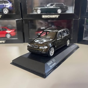 May include: A dark green 1:43 scale diecast model of a BMW X5 on a black display base. The base has the text "BMW X5" and "Oliy metallic" printed on it.