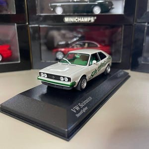 May include: White Volkswagen Scirocco Streetfighter diecast model car on a black display base. The car has green and white graphics and the text "VW Scirocco Streetfighter" is printed on the base.
