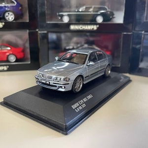 Puede incluir: Un coche modelo BMW E39 M5 5.0 V8 32V de 2003 de color plateado sobre una base de exhibición negra. El coche tiene ruedas negras y un interior negro. La base tiene el texto "BMW E39 M5 2003 5.0 V8 32V" impreso en ella.