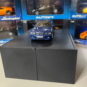 Puede incluir: Un coche modelo azul a escala 1:18 de un BMW M3 E46. El coche está en un expositor negro. El coche tiene un interior negro y ruedas negras. El coche tiene una matrícula que dice "M-Y3 6513".