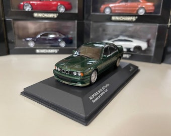 May include: A dark green 1/18 scale diecast model car of an Alpina B10 Biturbo based on a BMW E34. The model is displayed on a black base with the text "ALPINA B10 Biturbo Based on BMW E34".