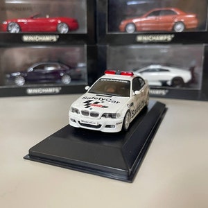 May include: White BMW M3 safety car model with black and red accents. The car has the words "Safety Car" and "Medical Car" printed on the side. The model is on a black display base.