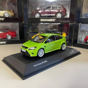May include: A lime green Ford Focus RS MKII model car on a black display stand. The model features silver wheels and a black spoiler. The stand is labelled "Ford Focus RS MKII". Other model cars are visible in the background.