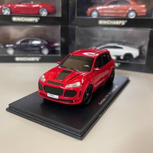 May include: A red 1:18 scale model of a Porsche Cayenne GTS with a black hood scoop and black wheels. The model is displayed on a black base with the text "Cayenne GTS Turbo S" printed on it.