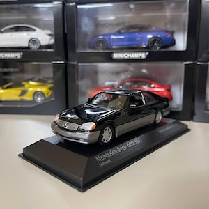 May include: A black Mercedes-Benz 600 SEC diecast model car on a black display base. The car has a silver trim and is labeled "Mercedes-Benz 600 SEC Schwarz".