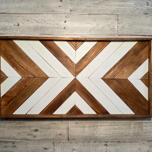 May include: A wooden wall decor with a geometric pattern of white and brown chevron shapes. The decor is framed in a dark brown wood frame.