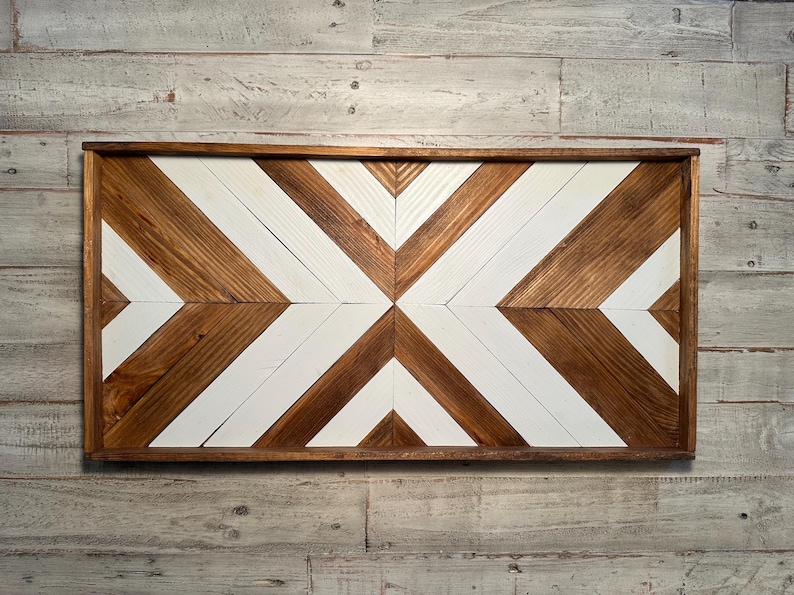 May include: A wooden wall decor with a geometric pattern of white and brown chevron shapes. The decor is framed in a dark brown wood frame.