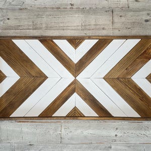 May include: A wooden wall decor with a geometric pattern of white and brown chevron shapes. The decor is framed with a dark brown wood frame.