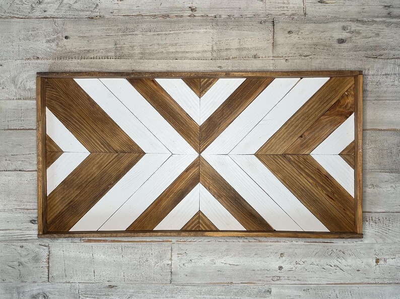 May include: A wooden wall decor with a geometric pattern of white and brown chevron shapes. The decor is framed with a dark brown wood frame.
