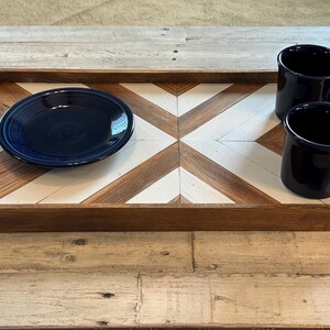 May include: A wooden serving tray with a geometric pattern of brown and white squares. The tray has two blue ceramic mugs and a blue ceramic plate on it.