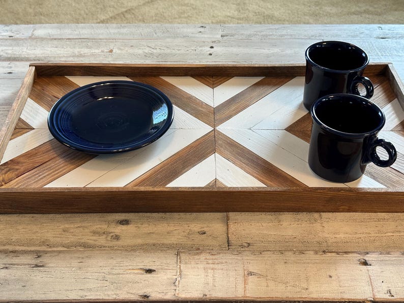 May include: A wooden serving tray with a geometric pattern of brown and white squares. The tray has two blue ceramic mugs and a blue ceramic plate on it.
