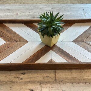 May include: A wooden tray with a chevron pattern in brown and white. A small succulent plant in a yellow pot sits in the center of the tray.