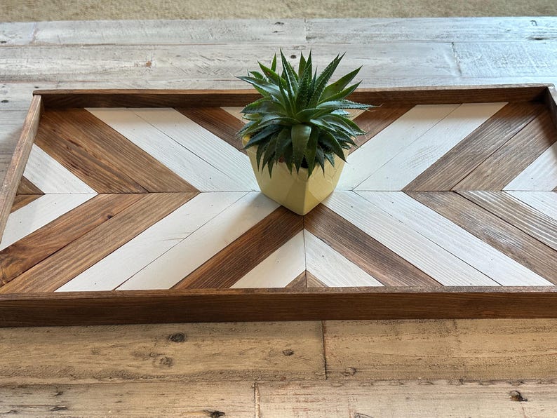 May include: A wooden tray with a chevron pattern in brown and white. A small succulent plant in a yellow pot sits in the center of the tray.