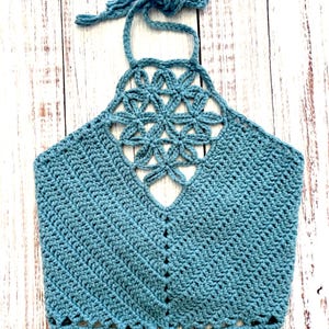 May include: A teal-colored, handmade crochet halter top. The top features a floral design at the neckline and a scalloped edge at the bottom. The halter straps are tied at the back of the neck.