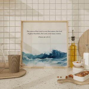 May include: A framed print with a watercolor painting of a blue wave crashing against a white background. The print has a white border and the text "The voice of the Lord is over the waters; the God of glory thunders, the Lord, over many waters. PSALM 29:3" printed in black.
