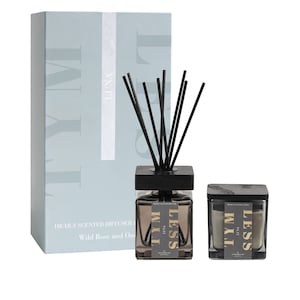 May include: A light blue box with the word "Luna" and the word "TYM" written vertically. The box contains a black diffuser bottle with black sticks and a black and gray candle. The candle and diffuser bottle both have the words "LESS" and "TYM" written on them.