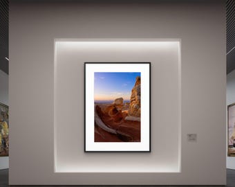May include: A framed landscape photograph of a desert scene with red rock formations under a blue sky. The photograph is displayed in a gallery setting, mounted on a white wall with recessed lighting.
