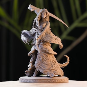 May include: A detailed, gray figurine of a female figure holding a scythe. The figure is wearing a long, flowing gown with a feathered texture. The figurine is standing on a circular base, with a blurred green background.