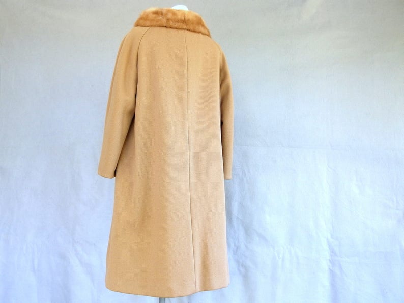 Back of vintage 1950's light brown, fur collared Holly Gab winter coat with a light brown mink fur collar & a double breasted front. There are 2 hooks on the removable collar that will snug the blonde fur, with a snap underneath. The front buttons. The 3/4 length sleeves are cut-on with a seam down the outside as well as the usual one underneath. There are 2 pockets in the front side seams with faux welts. It is lined with satin that has a backing of what looks like a loosely woven gray wool.