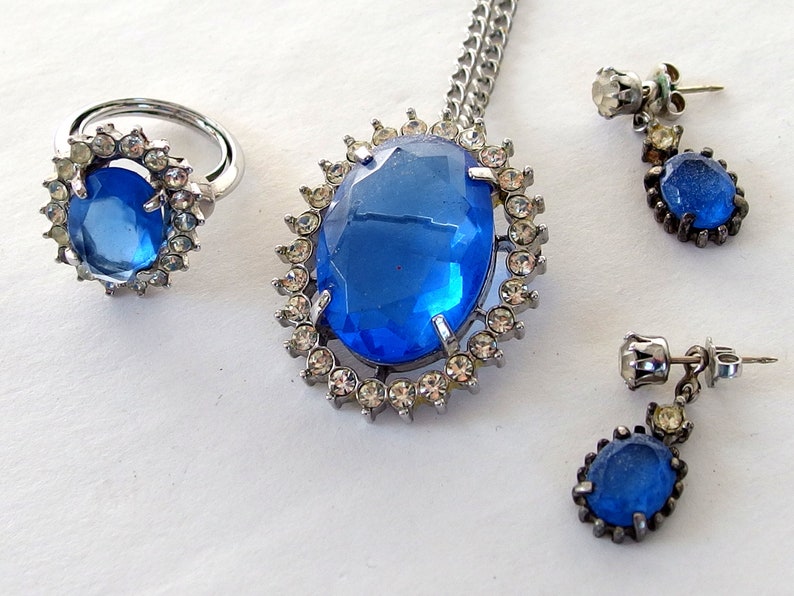 vintage Avon blue crystal glass set includes a necklace whose pendant may be used as a brooch, an adjusting ring, and a pair of dangle post earrings.
