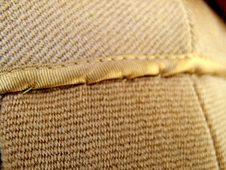 May include: Close-up of a beige fabric ribbon is sewn onto the fabric, creating a clean, finished edge. The image highlights the detail and craftsmanship of the textile.