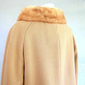 Back of vintage 1950's light brown, fur collared Holly Gab winter coat with a light brown mink fur collar & a double breasted front. There are 2 hooks on the removable collar that will snug the blonde fur, with a snap underneath. The front buttons. The 3/4 length sleeves are cut-on with a seam down the outside as well as the usual one underneath. There are 2 pockets in the front side seams with faux welts. It is lined with satin that has a backing of what looks like a loosely woven gray wool.