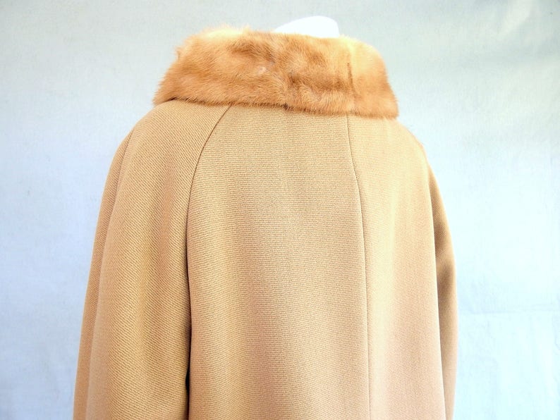 Back of vintage 1950's light brown, fur collared Holly Gab winter coat with a light brown mink fur collar & a double breasted front. There are 2 hooks on the removable collar that will snug the blonde fur, with a snap underneath. The front buttons. The 3/4 length sleeves are cut-on with a seam down the outside as well as the usual one underneath. There are 2 pockets in the front side seams with faux welts. It is lined with satin that has a backing of what looks like a loosely woven gray wool.