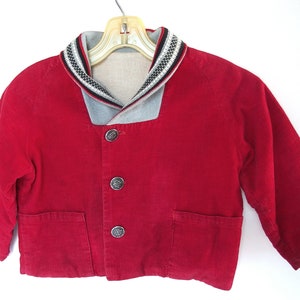May include: A red corduroy jacket with a grey and white striped collar. The jacket has four silver buttons down the front.