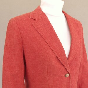 May include: A red blazer with a single button closure. The blazer is made of a textured fabric.