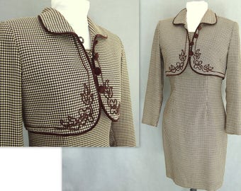 May include: A brown and white gingham dress with a matching brown and white gingham jacket. The jacket has a brown velvet trim and embroidered floral details.