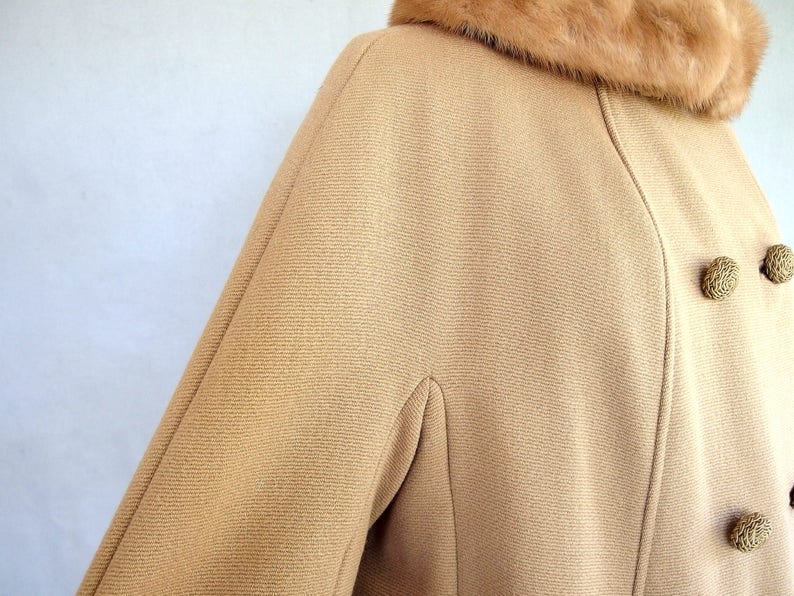 Vintage 1950's light brown, fur collared Holly Gab winter coat features a light brown mink fur collar & a double breasted front. There are 2 hooks on the removable collar that will snug the blonde fur, with a snap underneath. The front buttons. The 3/4 length sleeves are cut-on with a seam down the outside as well as the usual one underneath. There are 2 pockets in the front side seams with faux welts. It is lined with satin that has a backing of what looks like a loosely woven gray wool.