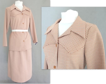 May include: A brown and white gingham skirt suit with a collared jacket and a long skirt. The jacket has a white belt and two pockets on the chest.