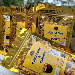 May include: Four gold foil bags of roasted corn and peanuts snack. The bags are labeled "Roasted Corn & Peanuts".