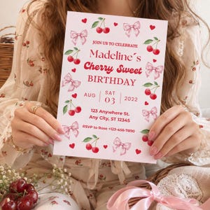Op de afbeelding: Een rechthoekige verjaardagsuitnodigingskaart met een witte achtergrond, voorzien van rode kersenillustraties, roze strikken en kleine rode hartjes. De tekst luidt: JOIN US TO CELEBRATE Madeline's Cherry Sweet BIRTHDAY AUG SAT 03 2022 123 Anywhere St. Any City, ST 12345 RSVP to Rose +123-456-7890.