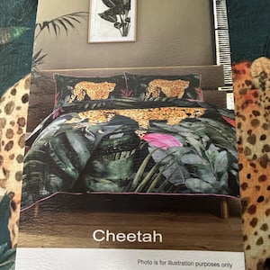 May include: A bedding set featuring a quilt and two pillowcases with a jungle theme, displaying cheetahs amidst large green tropical leaves and pink floral accents. The word Cheetah is printed at the bottom of the image, along with the text Photo is for illustration purposes only.