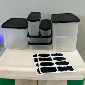 Könnte beinhalten: Ein Set aus fünf durchscheinenden Kunststoff-Vorratsbehältern mit schwarzen Deckeln in verschiedenen rechteckigen Größen, begleitet von einem Bogen mit zwölf schwarzen Klebeetiketten in verschiedenen dekorativen Formen zur Organisation.
