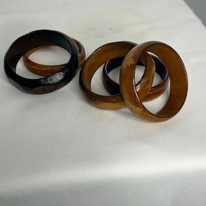 Puede incluir: Un conjunto de cuatro brazaletes circulares de madera en varios tonos de marrón. Un brazalete es de color espresso oscuro, mientras que los otros presentan tonos miel y bronceado con vetas de madera visibles y detalles de incrustaciones.
